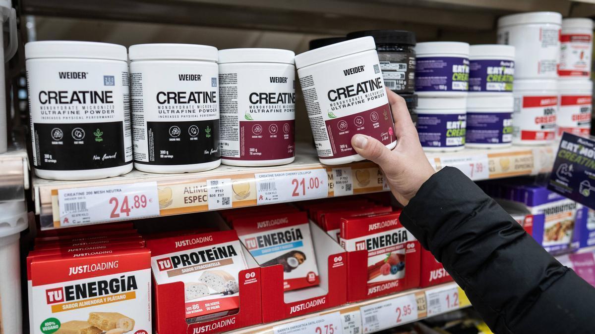 Un comprador compara diferents marques de creatina en un supermercat.