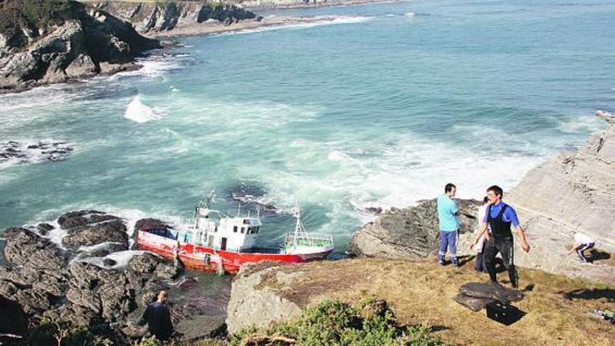 Marineros, ayer, recogiendo piezas de «La Polar», que aparece encallado entre las rocas.