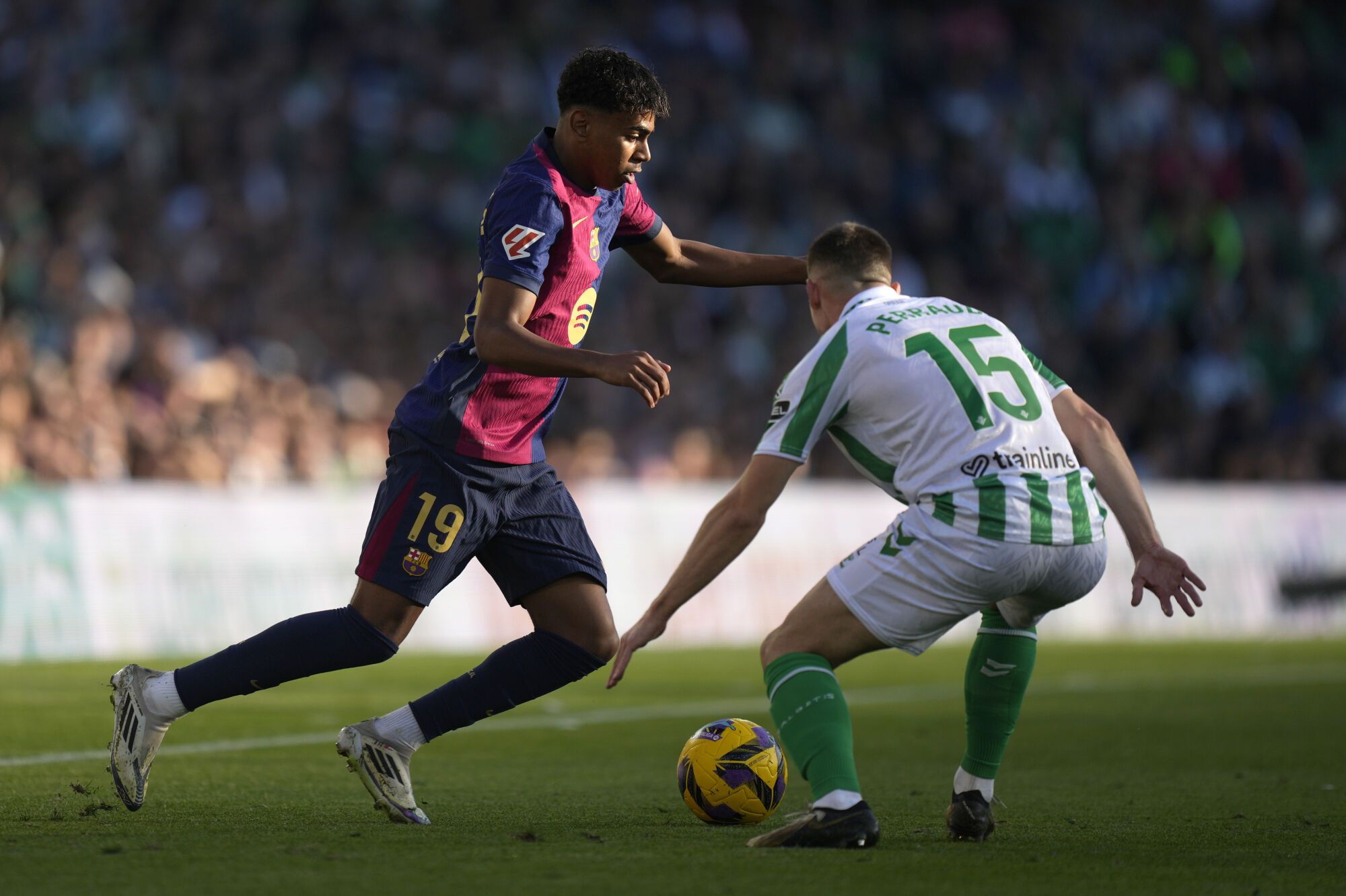 Barcelona&#039;s Lamine Yamal, left, challenges for the ball with Betis&#039; Romain Perraud during a Spanish La Liga soccer match between Betis and Barcelona at the Benito Villamarin stadium in Seville, Spain, Saturday, Dec. 7, 2024. (AP Photo/Jose Breton). EDITORIAL USE ONLY/ONLY ITALY AND SPAIN