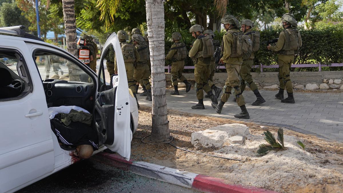 Soldados israelís pasan junto a un civil tiroteado en su vehículo por militantes palestinos en Sderot, Israel.