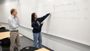 Divya Tyagi muestra su trabajo sobre un problema matemático de hace un siglo a Sven Schmitz, miembro de la facultad de la Facultad de Ingeniería y asesor de Tyagi.