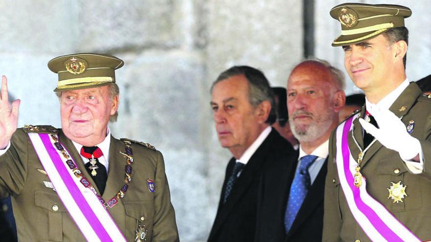 El rey Juan Carlos y el príncipe Felipe saludan a los asistentes antes de retirarse de la tribuna tras el acto castrense en El Escorial.