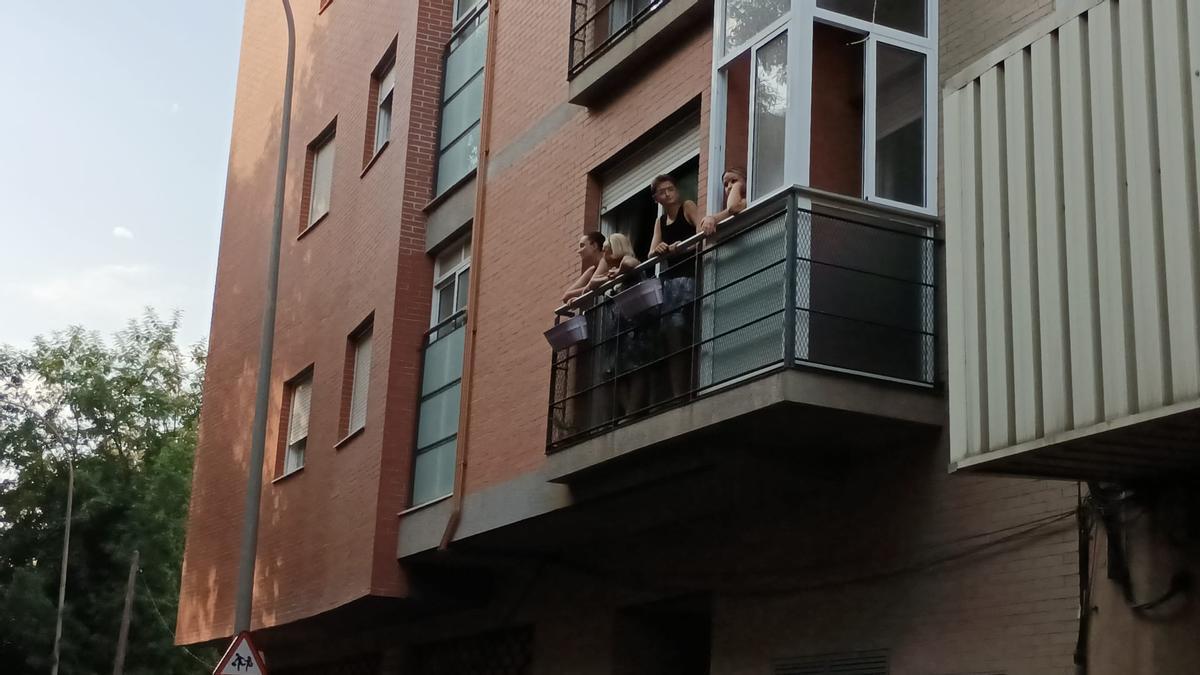 Varias personas se asoman por el balcón de una casa.