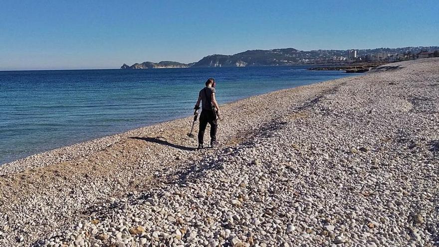 Un joven buscador de «tesoros» rastrea con el detector de metales la playa del Benissero de Xàbia.