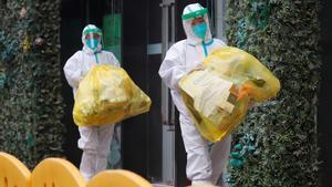 Dos personas con el equipo de protección completo contra el coronavirus en el exterior del hotel donde se han alojado en Wuhan los investigadores de la OMS.