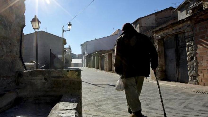 Un hombre pasea bien abrigado esta mañana en la localidad castellonense de Barracas, donde a pesar del sol una fuente aún permanece helada por las bajas temperaturas nocturnas.