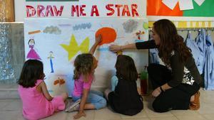 Una maestra de infantil ayuda a sus alumnos a terminar un póster en inglés en un colegio de Barcelona.