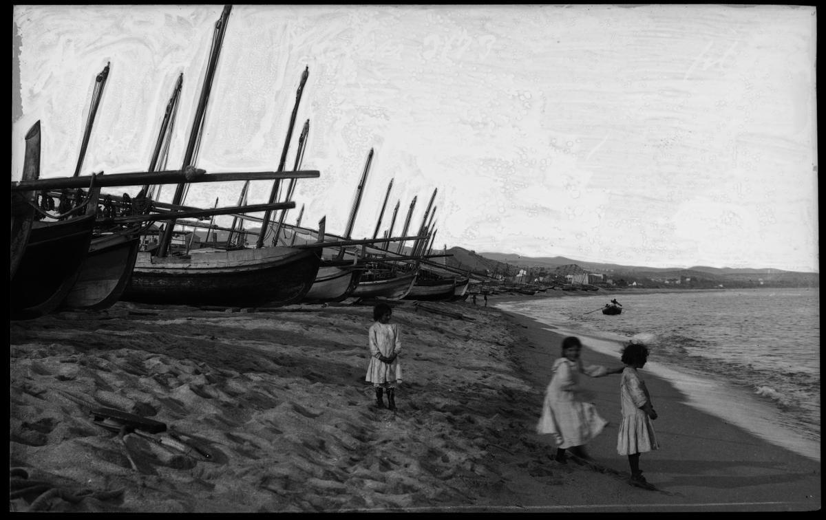 Tres niñas esperan la llegada de barcas en la playa de Mataró.