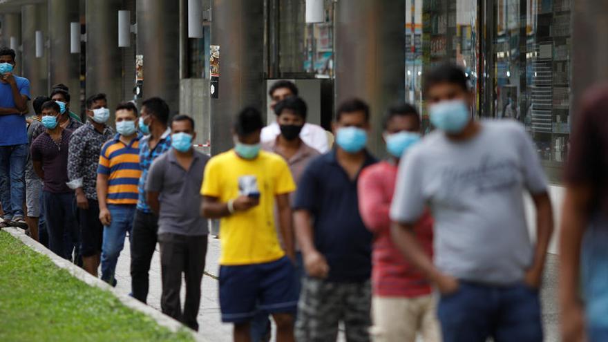 Trabajadores migrantes esperan a los voluntarios para distribuir comidas gratuitas en Singapur.