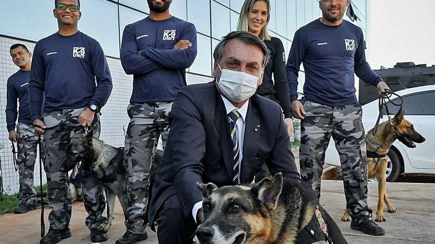 Bolsonaro posa con mascarilla junto a un perro y varios policías sin protección, antes de un acto en Brasilia.