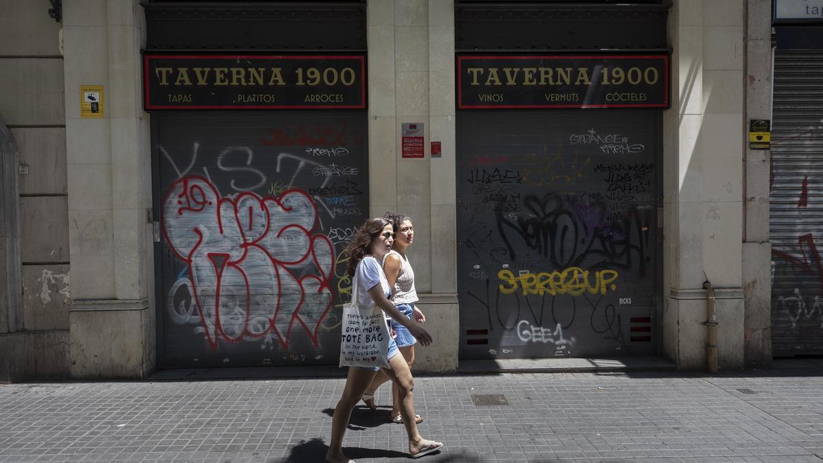 Dos personas caminan frente a un bar cerrado en Barcelona.