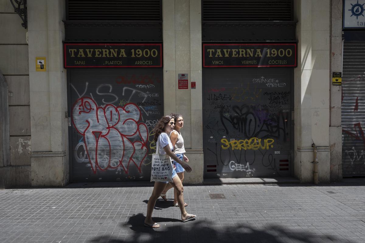 Dos personas caminan frente a un bar cerrado en Barcelona.