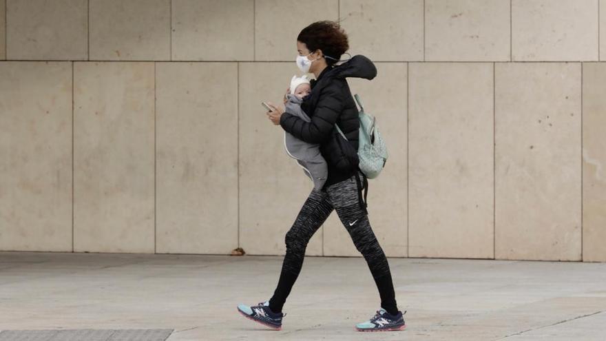 Una mujer con un bebé camina con el viento en contra frente al Palacio de Congresos de Palma