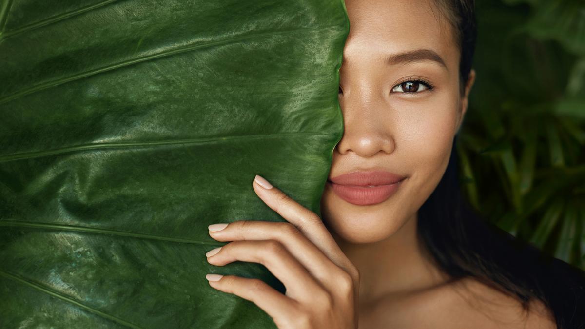 Chica con media cara escondida detrás de una hoja gigante