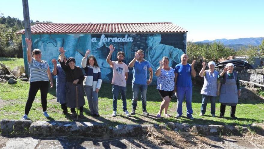 Un grupo de vecinos y operarios posa en la Eira da Carballa, frente a una de las construcciones recuperadas con nueva cubierta y uno de los murales dedicados al ciclo del pan.    | // FERNANDO CASANOVA