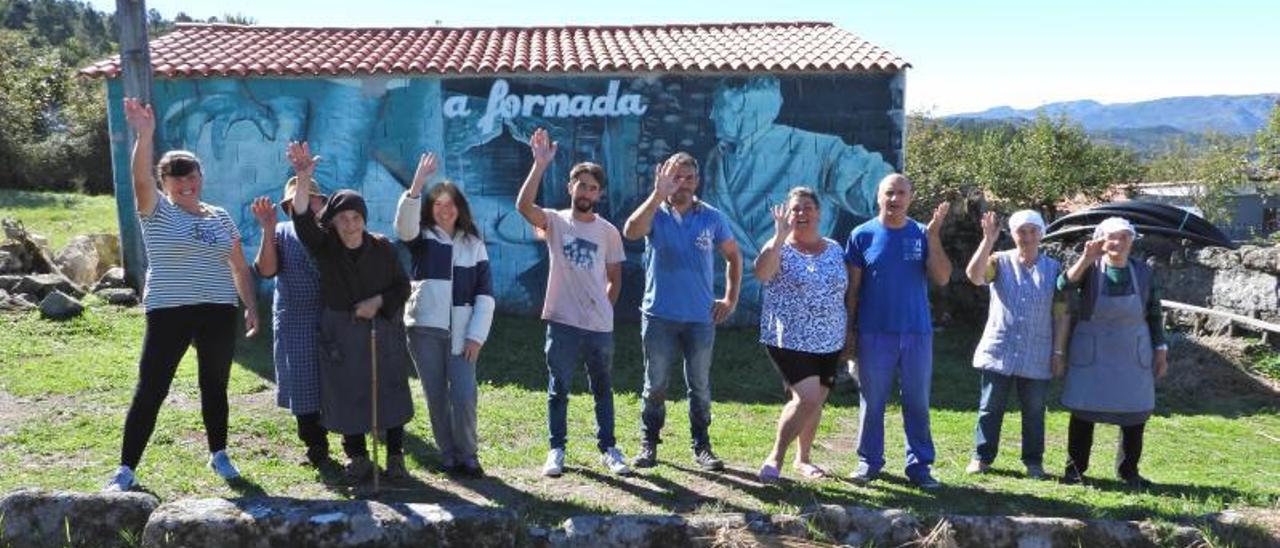 Un grupo de vecinos y operarios posa en la Eira da Carballa, frente a una de las construcciones recuperadas con nueva cubierta y uno de los murales dedicados al ciclo del pan.    | // FERNANDO CASANOVA