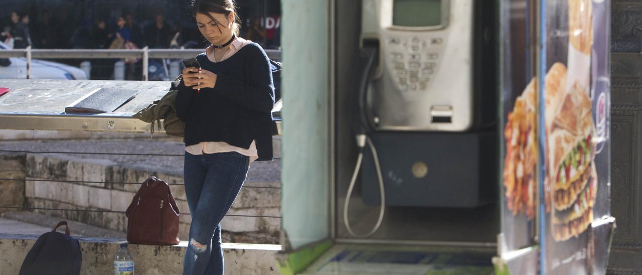 Una jove mira el seu telèfon mòbil al costat d&#039;una cabina telefònica.