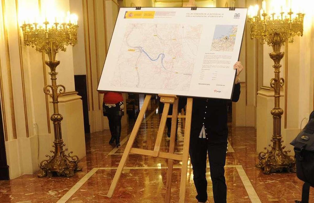 Una funcionaria traslada el cartel con el trazado del vial 18 cuando se anunció en A Coruña en 2015.