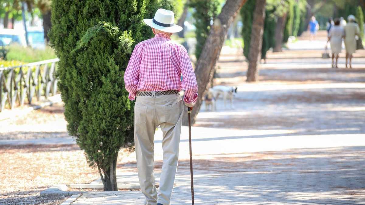 Un anciano pasea solo, apoyándose en su bastón
