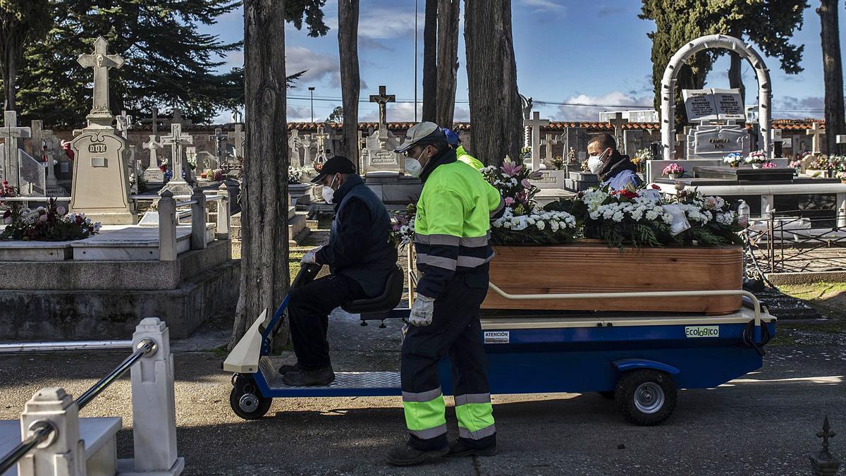 Los operarios del cementerio trasladan en una plataforma mecánica el féretro de una mujer centenaria fallecida por COVID, enterrada este sábado. | Emilio Fraile