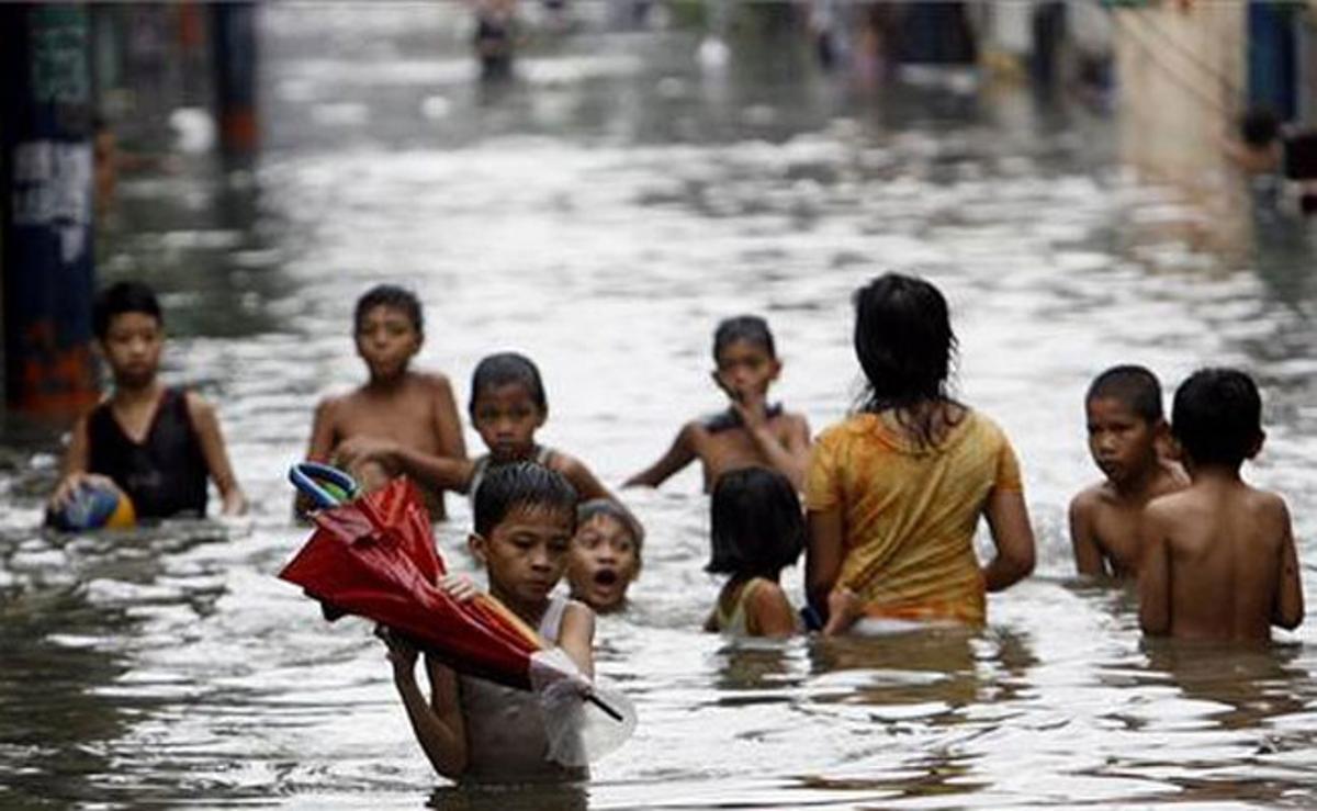 Diversos nens intenten travessar un carrer inundat per les pluges del tifó ’Muifa’ a Quezon City (Filipines).