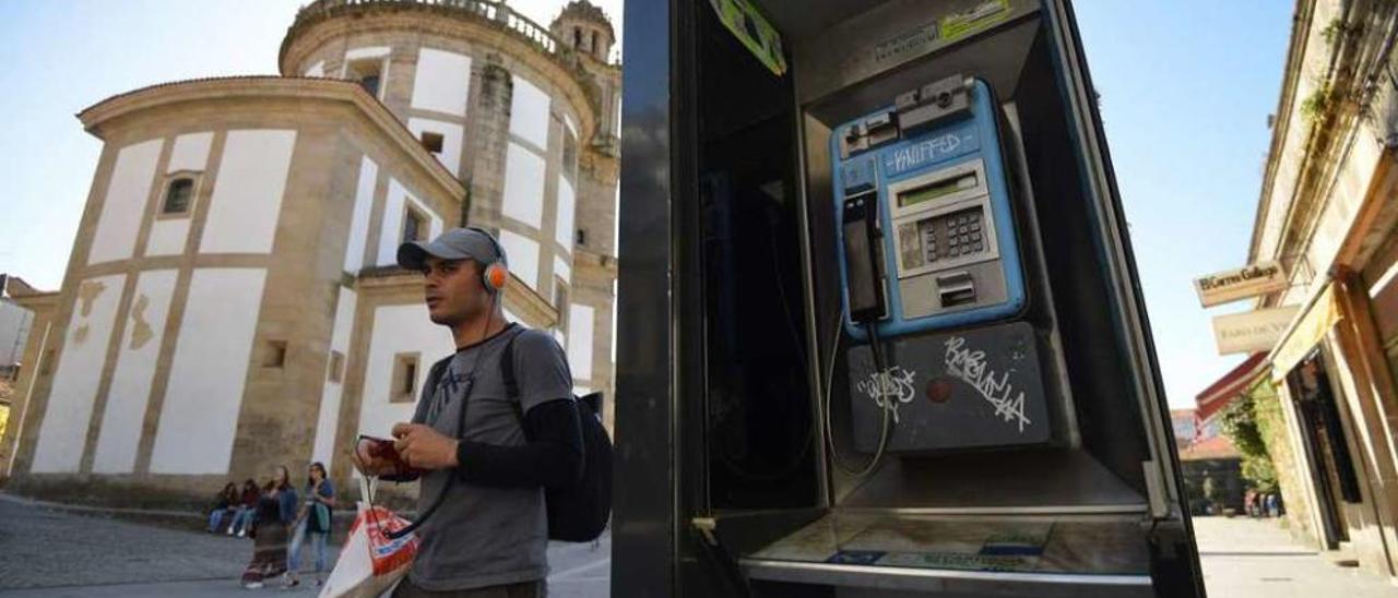 Un joven, con su smartphone en la mano, pasa tras la cabina telefónica de la Praza da Peregrina. // G.S.