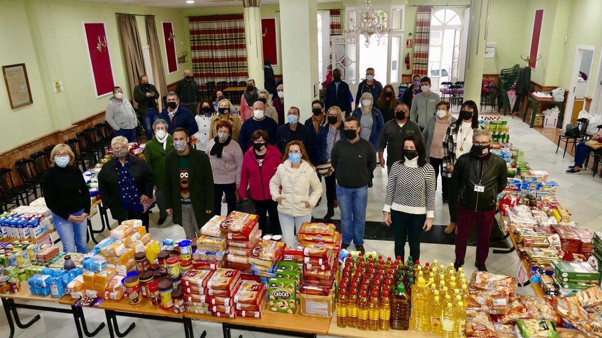 Asistentes al segundo desayuno solidario junto a todos los alimentos recaudados.