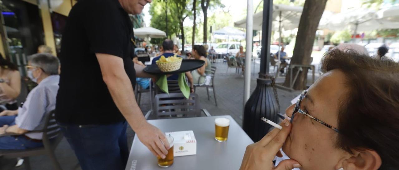 Una mujer fuma en la terraza de un bar de Córdoba, mientras una camarero sirve unas cervezas.