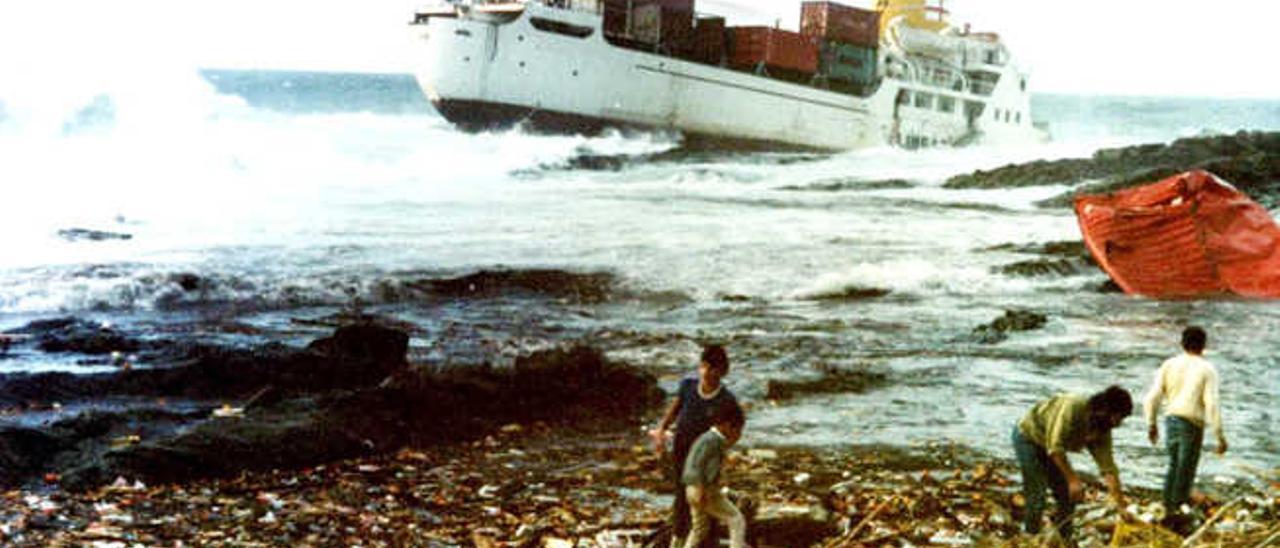 Un grupo de vecinos recoge los productos arrojados por el mar en la playa del Valle, al fondo el &#039;Júcar&#039; encallado