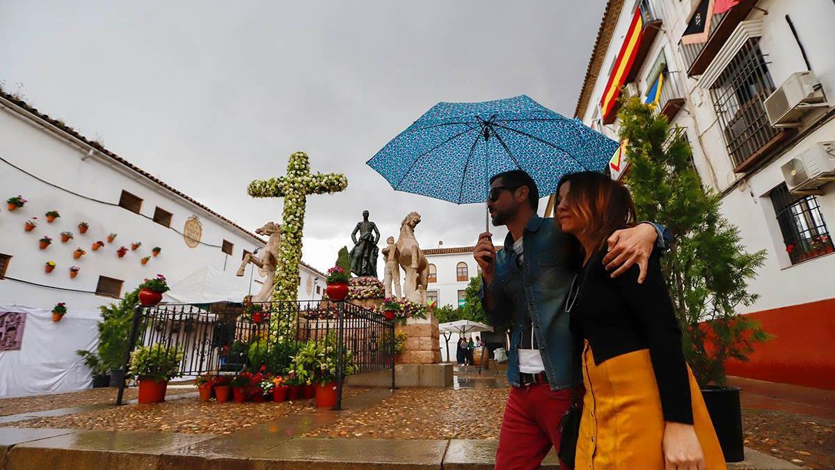 Dos jóvenes pasean frente a la Cruz de Santa Marina en un día lluvioso.
