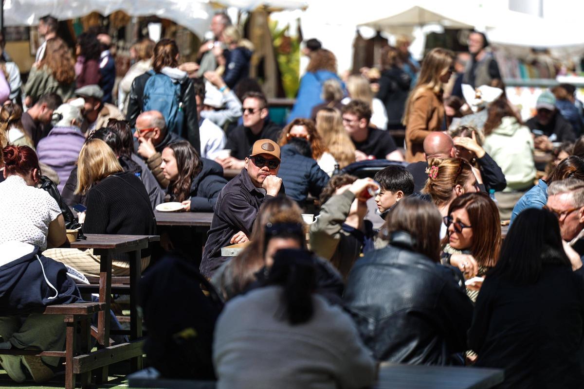 Turistas comiendo y disfrutando del sol en los bancos del mercadillo.
