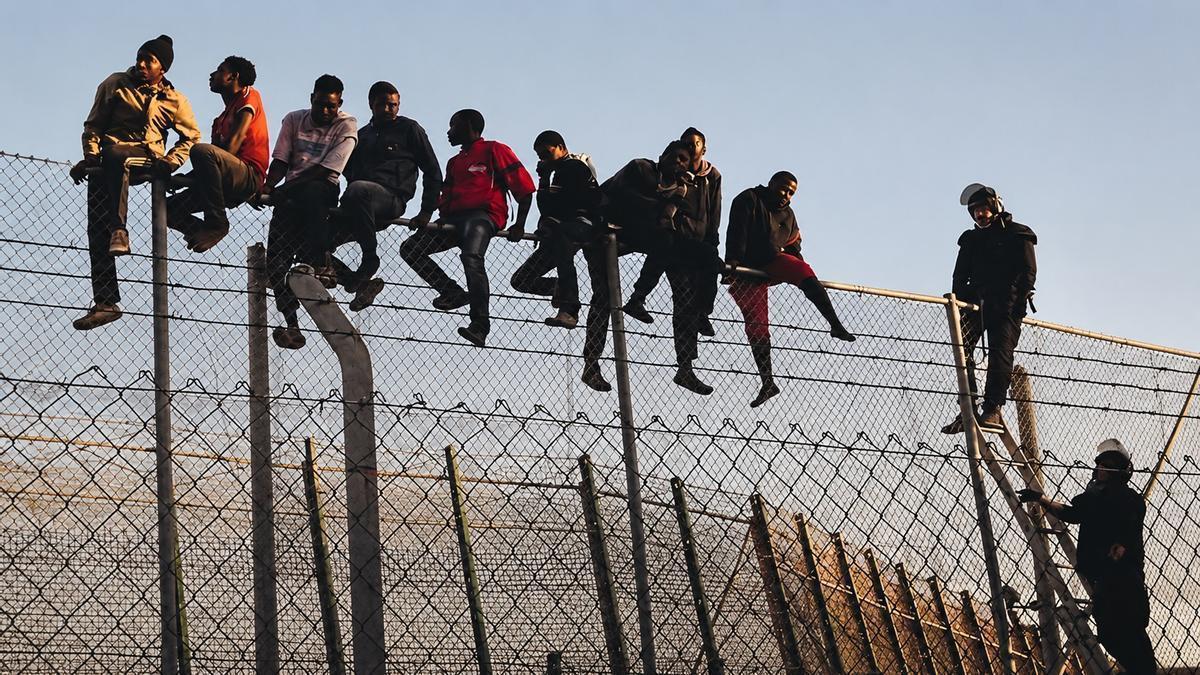Policías españoles tratan de disuadir a inmigrantes encaramados a la valla de Melilla.