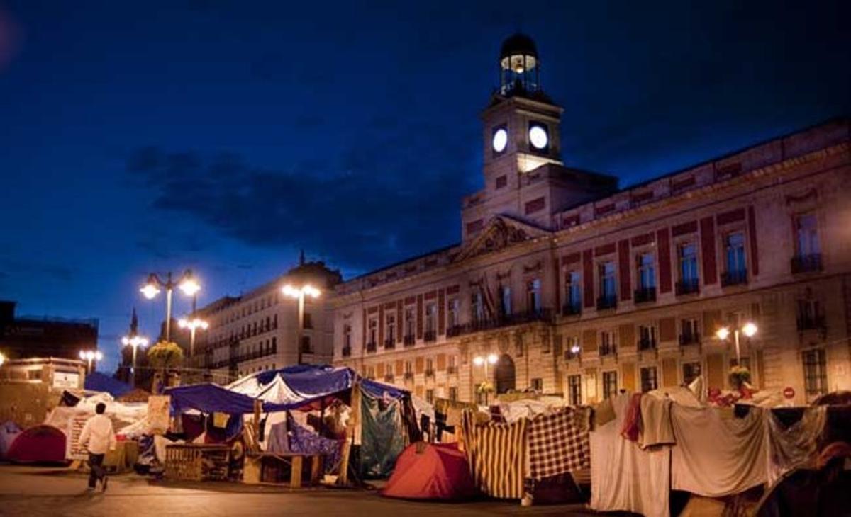 Un home passeja a prop de les tendes dels acampats a la Puerta del Sol, a Madrid, de matinada.