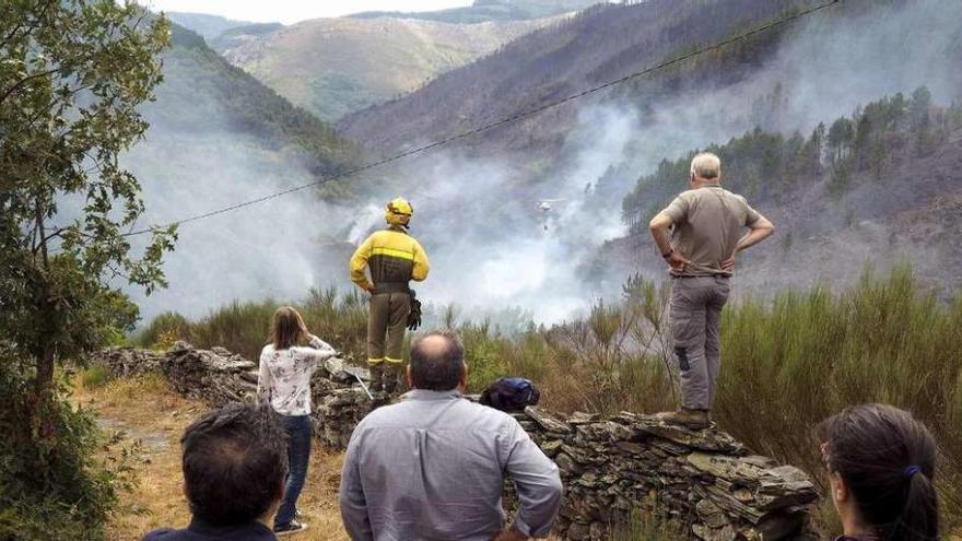 Un brigadista y vecinos siguen la evolución del incendio de Navia de Suarna.