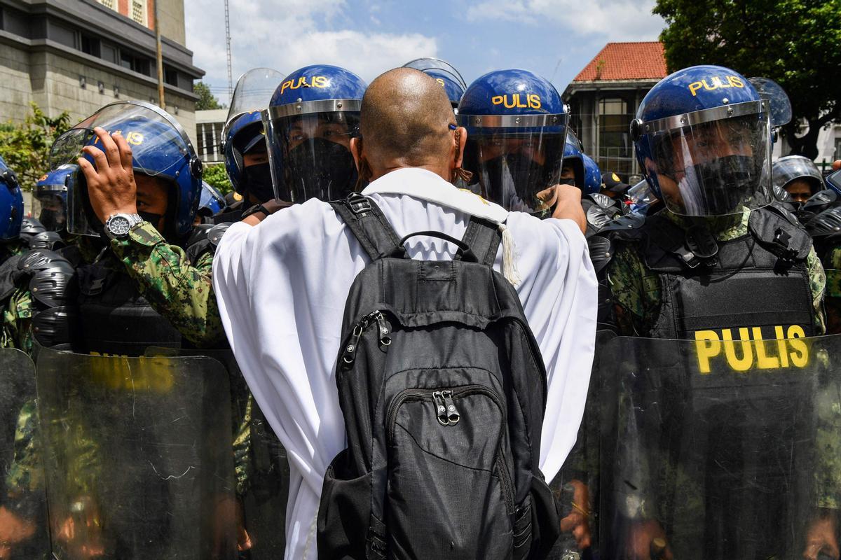 Un sacerdote católico trata de hablar con los agentes de la policía mientras numerosos manifestantes expresan su descontento frente a la Comisión de las Elecciones, en Manila