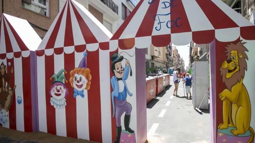 Una grúa se acerca al remate de la Hoguera Especial de Sagrada Familia. Al lado, portada de una barraca en Carolinas Altas.