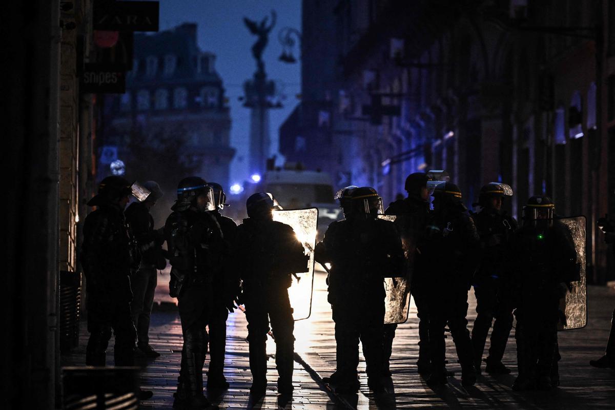 Los disturbios se extienden por Francia en la cuarta noche de protestas. Oficiales de la policía antidisturbios de Francia montan guardia después de que un grupo de manifestantes encendiera fuego en Burdeos