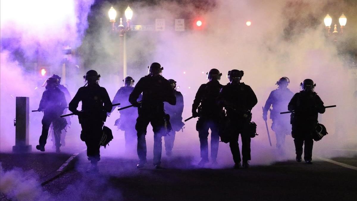 Policías caminan envueltos por gases lacrimógenos en Portland.