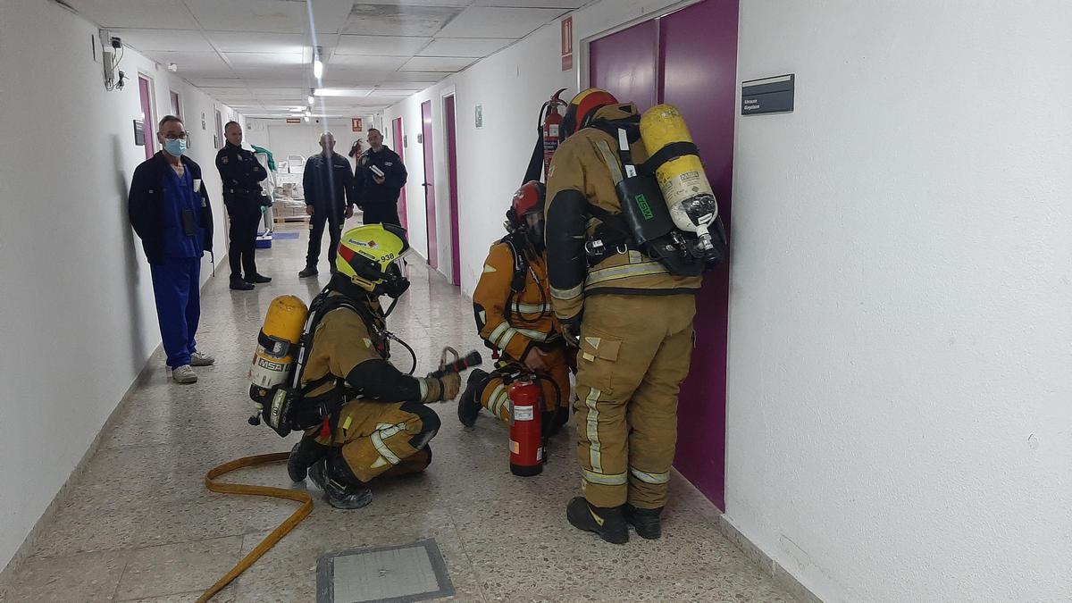 Bomberos simulando la apertura de una puerta del Hospital de Elche donde se encuentra un supuesto foco de incendio