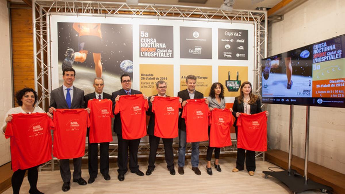 Los asistentes a la presentación de la 5ª Carrera Nocturna Sport Ciutat de L'Hospitalet mostrando la camiseta roja que lucirán los corredores.