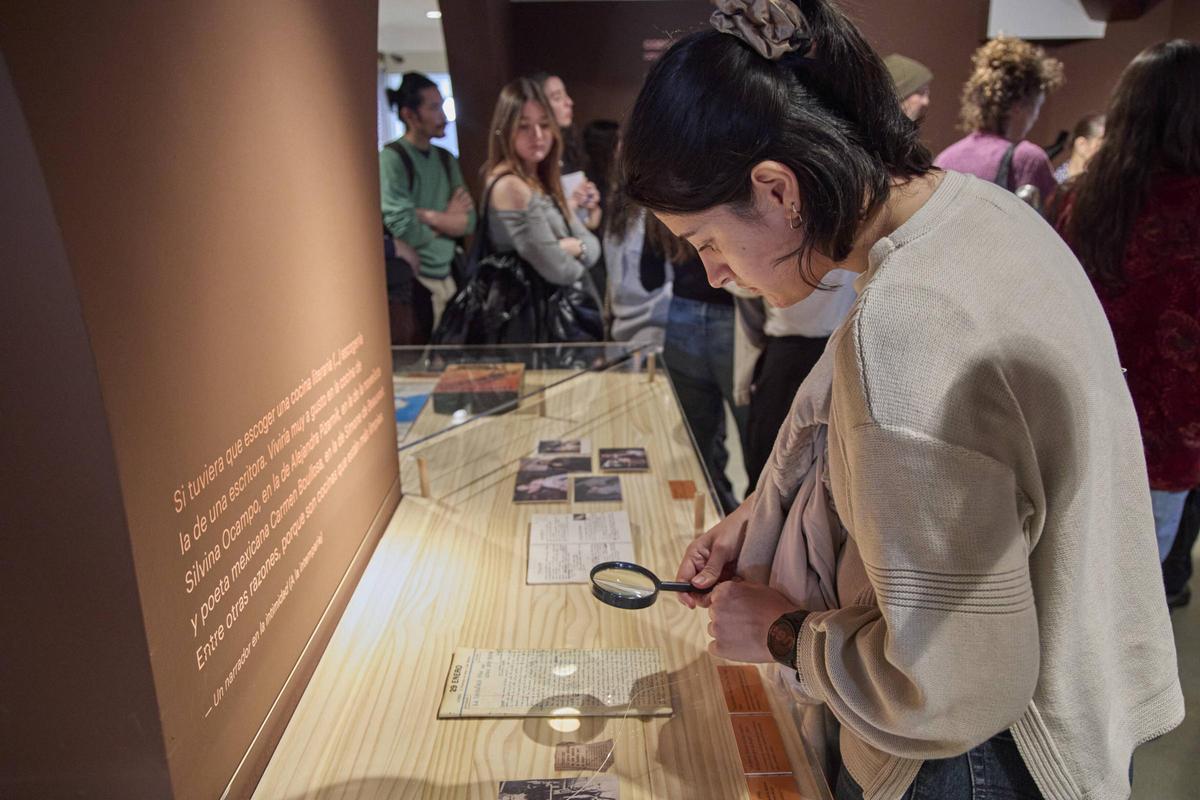 Una visitant llegeix un manuscrit amb ajuda d'una lupa.