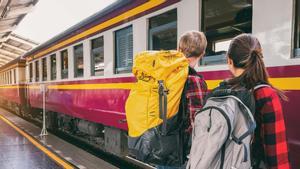Dos jóvenes cargados con mochilas esperan un tren en una estación europea.