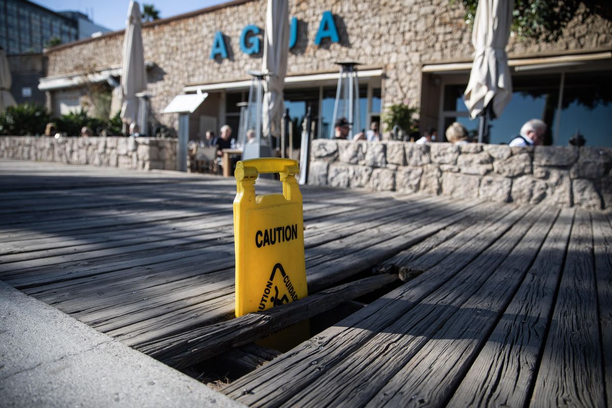 Un cartel de advertencia en unas tablas rotas, frente a la zona de restaurantes del paseo Marítim.