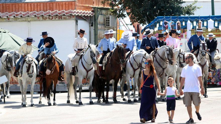 Una familia pasea frente a múltiples caballistas en el Real de la Feria.