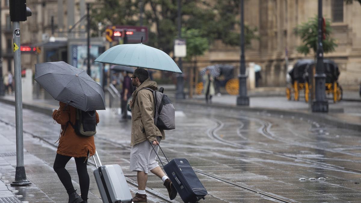 Archivo - Una pareja con maletas se protegen de la lluvia bajo sus paraguas. A 21 de octubre de 2022, en Sevilla (Andalucía, España). (Foto de archivo).