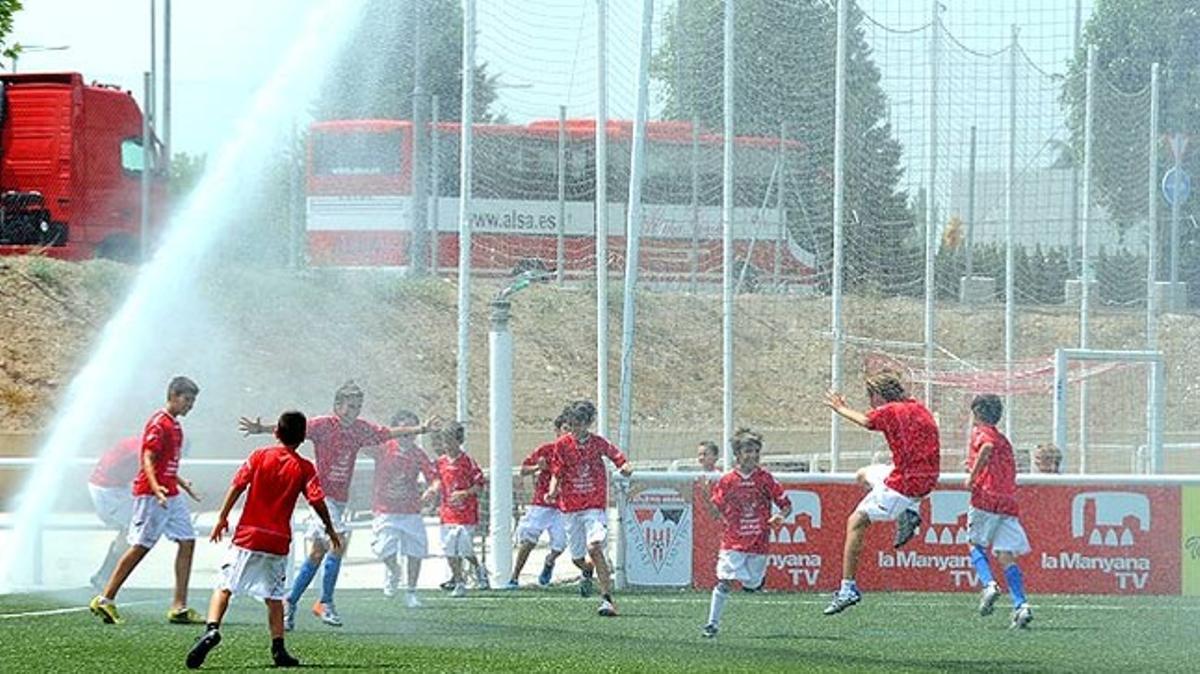 Un grupo de niños futbolistas del Atletic Segre de Lleida juega bajo las regaderas del campo.