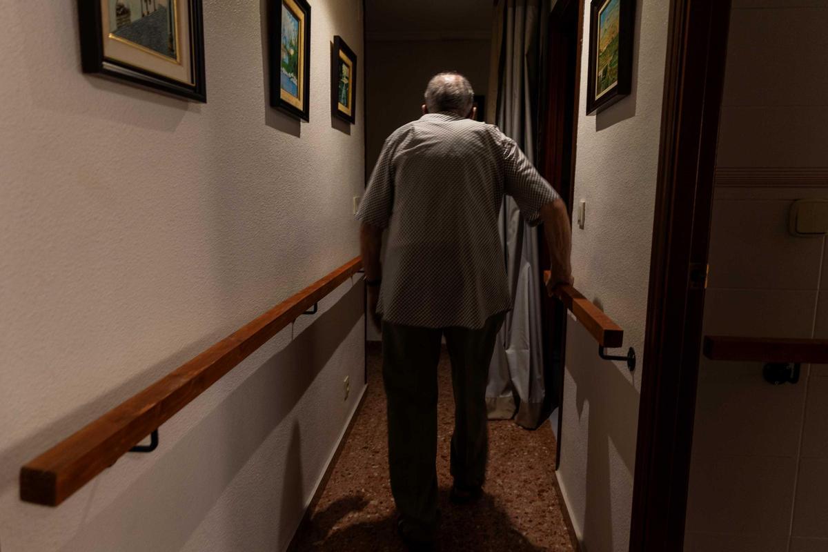 Una persona mayor camina por el pasillo de su casa, donde vive a solas.