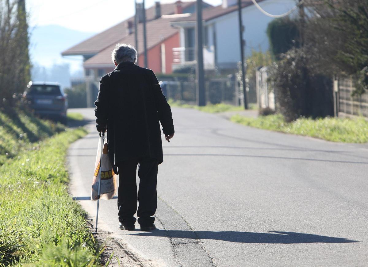 Un hombre mayor camina solo por una carretera hacia unas viviendas.