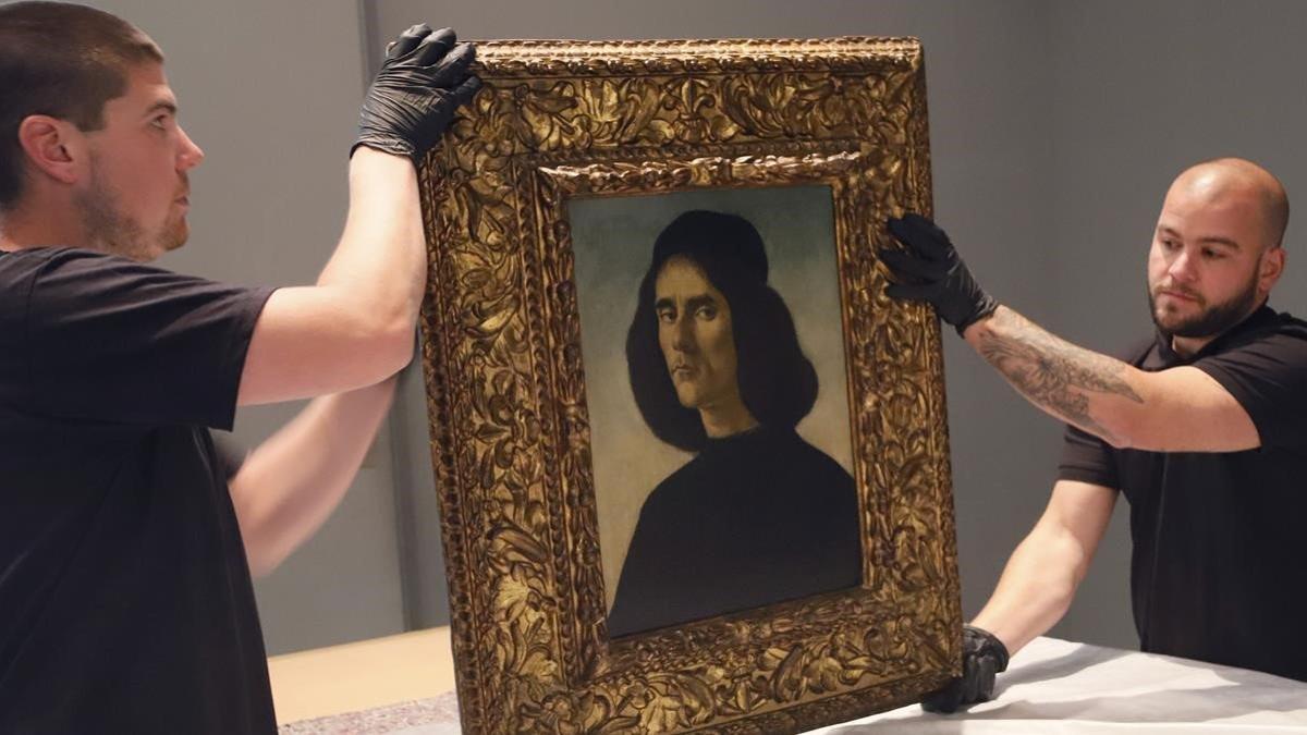 Dos personas sostienen el cuadro de Botticelli 'Retrato de Michele Marullo Tarcaniota'