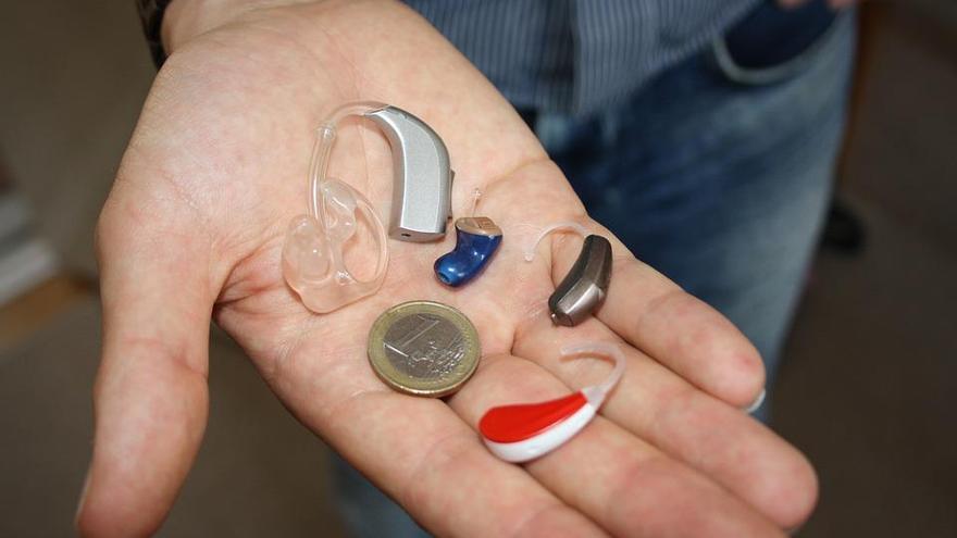 Un hombre compara el tamaño de varios audífonos con un euro.